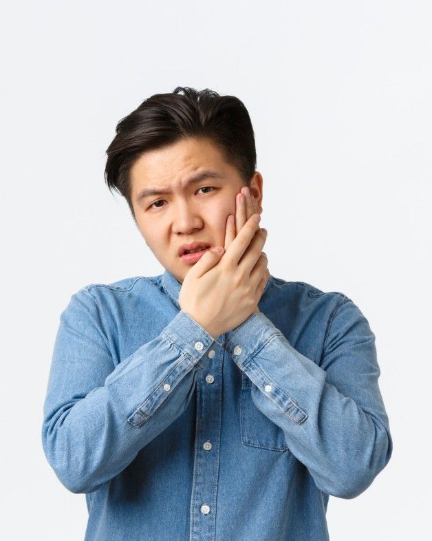 Man holding his cheek in discomfort after chipping or cracking a tooth, before visiting iCare Dental IOI City Mall Putrajaya