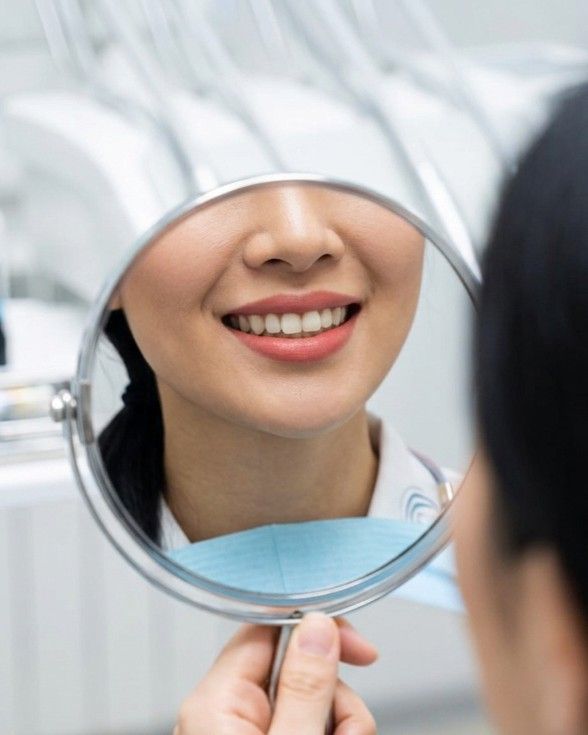 Patient admiring her clean, healthy smile in a hand mirror after a check-up at iCare Dental IOI City Mall Putrajaya